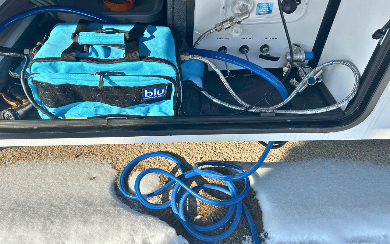 A heated hose hooked to a water filter in a fifth wheel underpass with snow on the ground below.